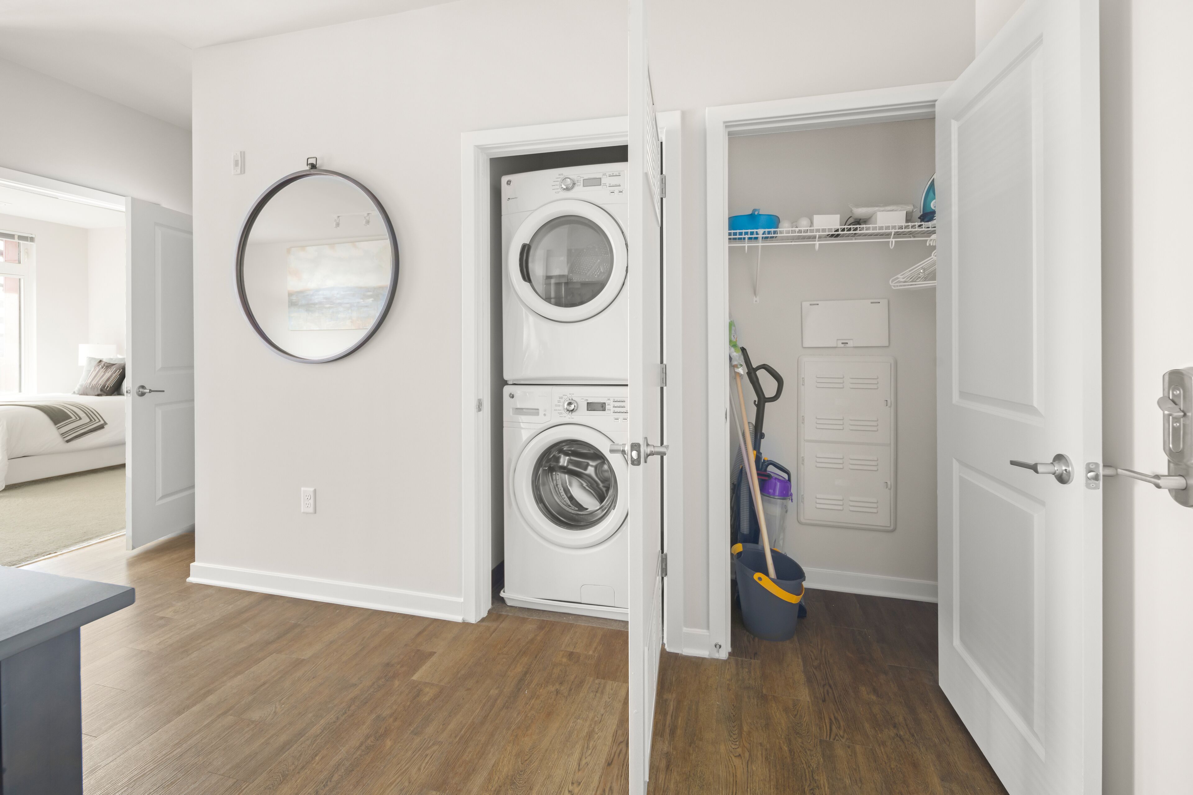 A laundry room with a front-loading washer and dryer, a mop, and a broom.
