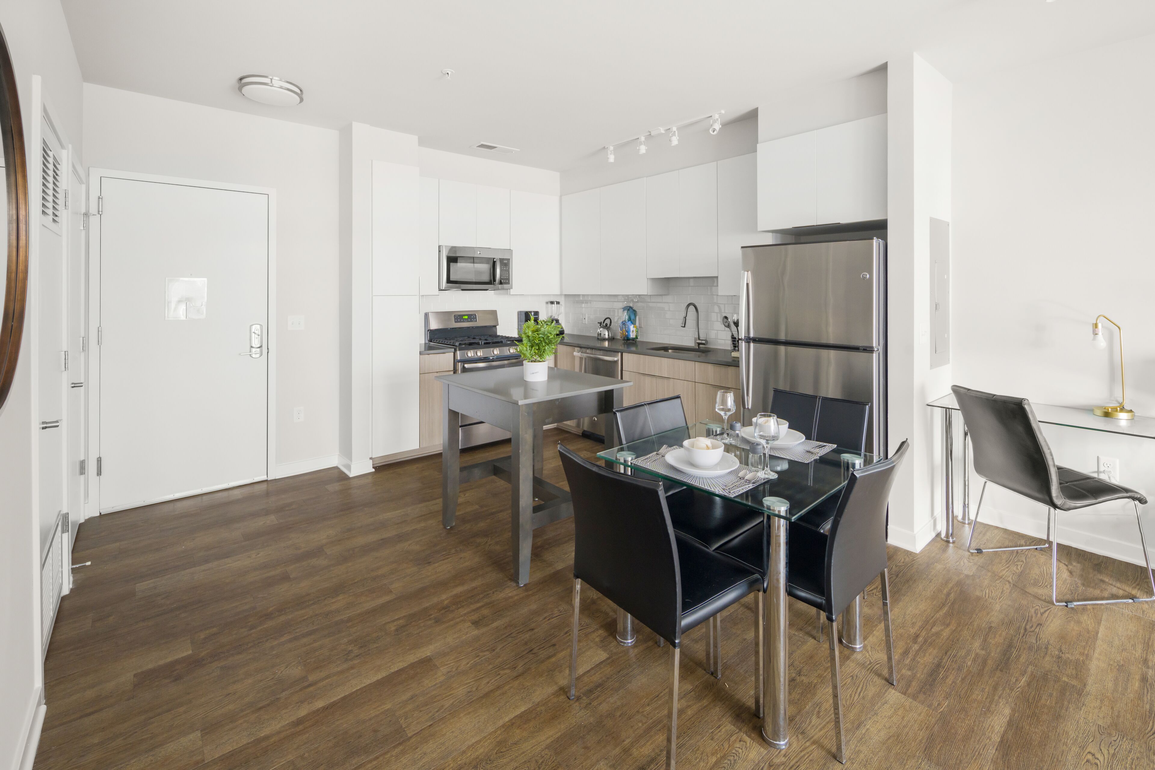 Een moderne keuken met witte kasten, roestvrijstalen apparatuur en een eethoek met een glazen tafel en zwarte stoelen.