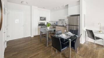 Een moderne keuken met witte kasten, roestvrijstalen apparatuur en een eethoek met een glazen tafel en zwarte stoelen.