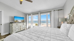A bedroom with a large bed, a dresser, a TV on the dresser, and a view of the beach through the windows. - Beachside West 13 (Panama City Beach)