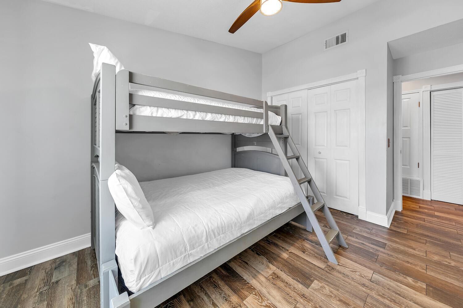 A bunk bed with a ladder, white walls, and wooden flooring.