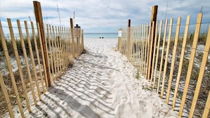 A sandy pathway leading to a beach, flanked by wooden fences and signs. - Aquavista 404e (Panama City Beach)