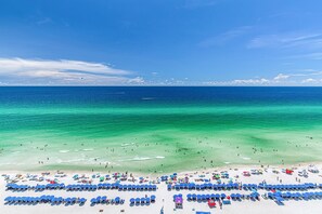 A beach with rows of blue umbrellas and beach chairs, clear turquoise water, and a sandy shore.