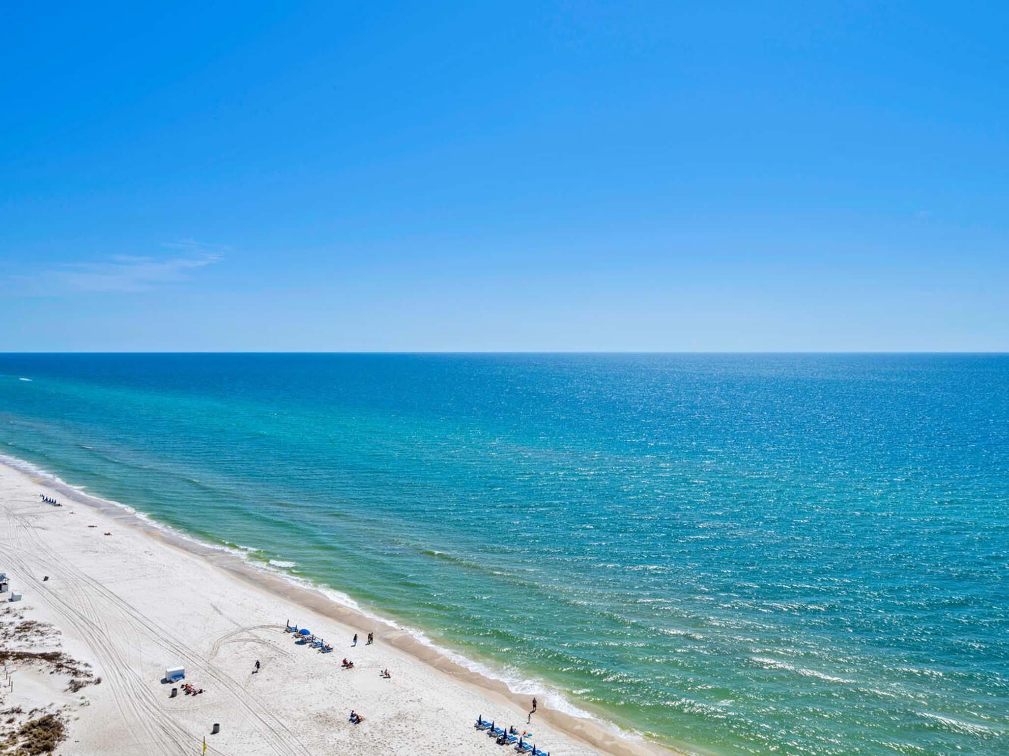 A beach with clear blue water, sandy shore, and a few beach chairs and umbrellas.