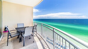 A balcony with a table and chairs overlooking a beach with clear turquoise water and a few boats. - Aqua Resort 1505 (Panama City Beach)