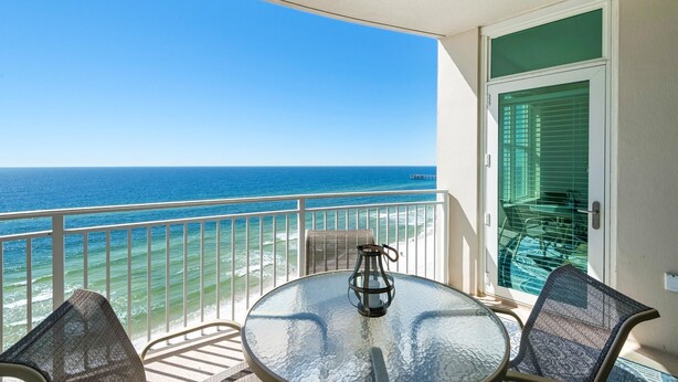 A balcony with a glass table, two chairs, and a lantern. - Aqua Resort 1007 (Panama City Beach)