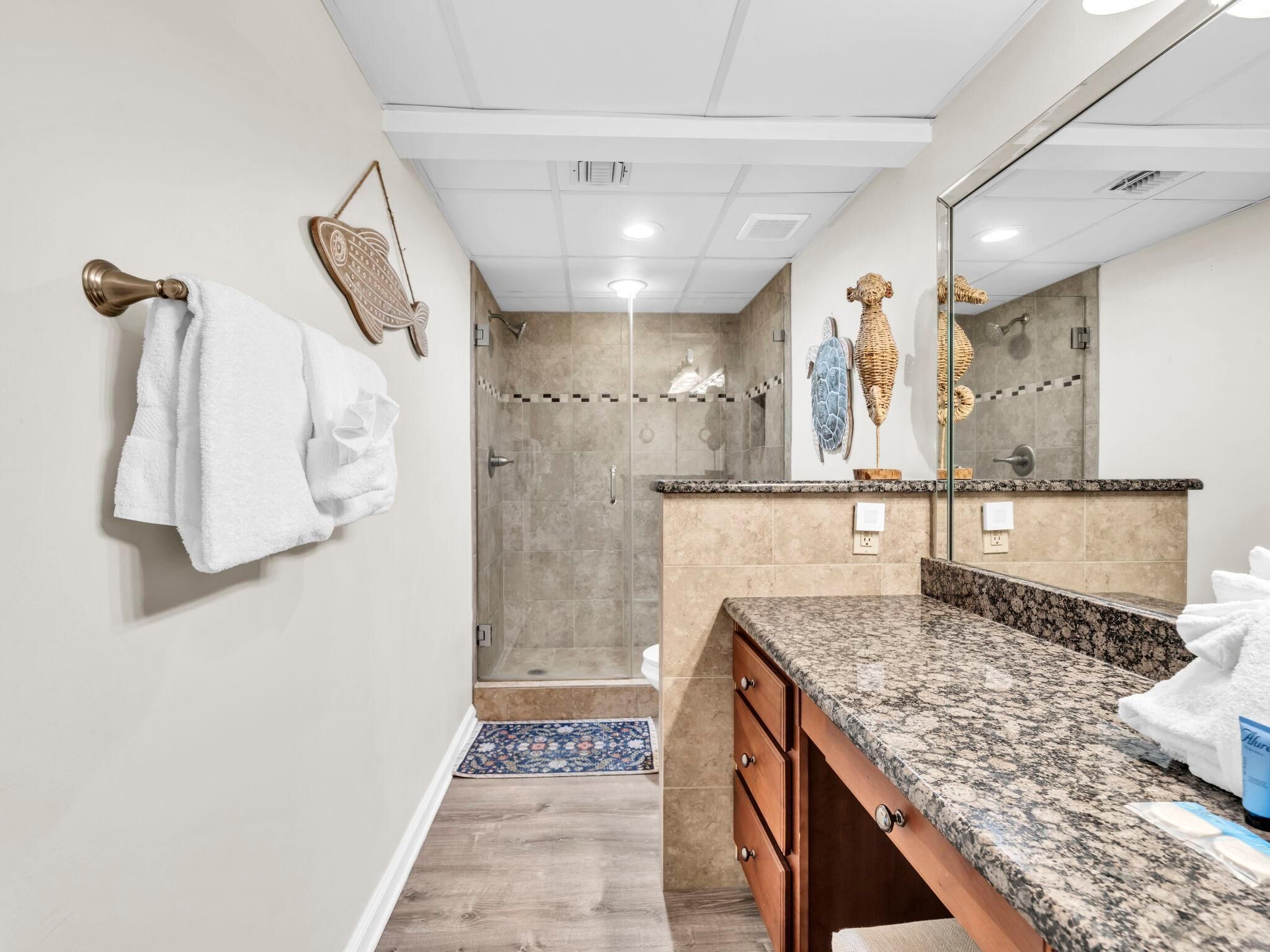 A modern bathroom with a walk-in shower, a large mirror, and a granite countertop.