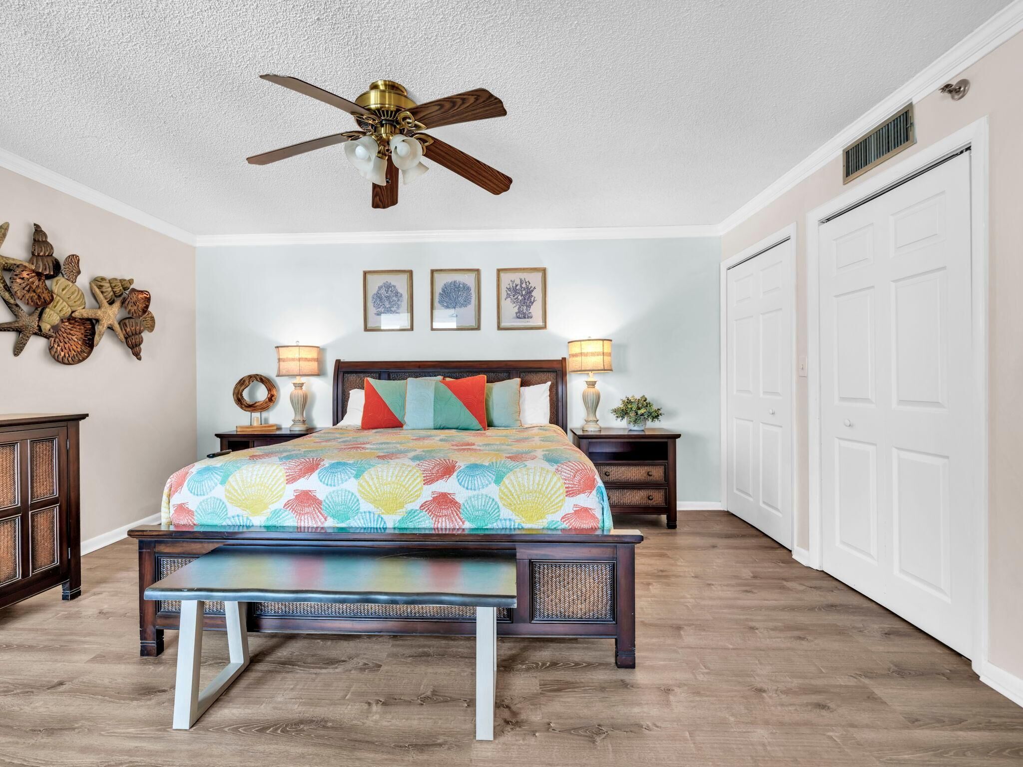 A bedroom with a wooden bed, a ceiling fan, a nightstand with lamps, and a large window.