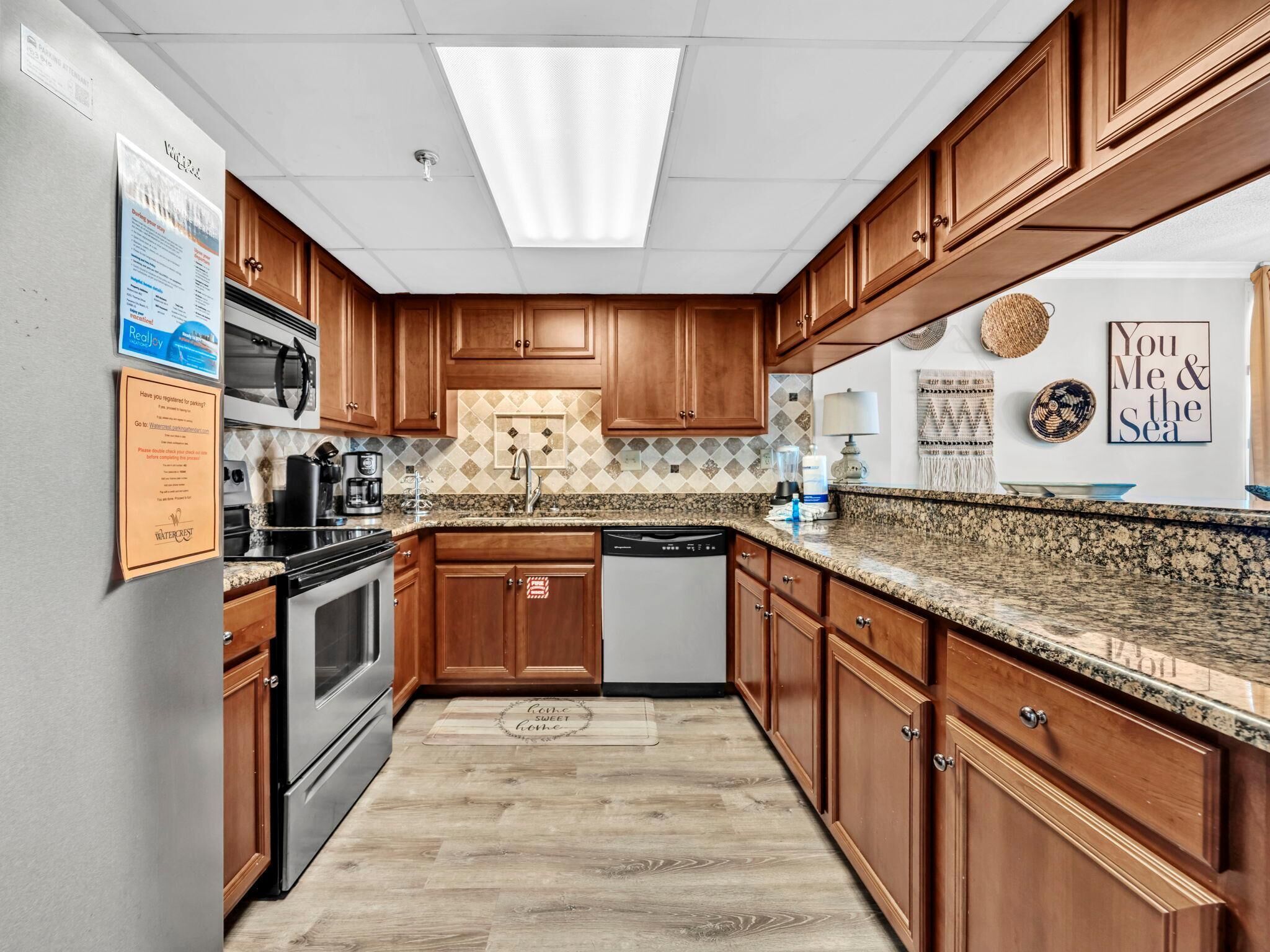 A kitchen with wooden cabinets, granite countertops, a stainless steel refrigerator, a microwave, a coffee maker, and a dishwasher.