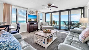 Un salon spacieux avec un grand canapé, une table basse et un téléviseur. Il y a un balcon avec vue sur l’océan.