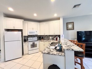 A kitchen with white cabinets, a microwave, an oven, a sink, and a marble countertop.
