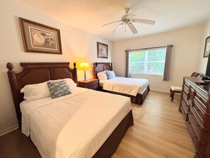 A hotel room with two beds, a ceiling fan, a window with blinds, and a dresser.