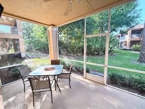 A covered patio with a table and chairs, large windows, and a view of a landscaped garden.