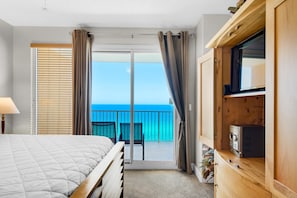Un dormitorio con cama, armario de madera, televisor y balcón con vista al océano.
