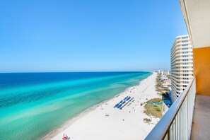A beach view from a balcony overlooking a hotel with a clear blue sky. - Treasure Island 1410 (Panama City Beach)