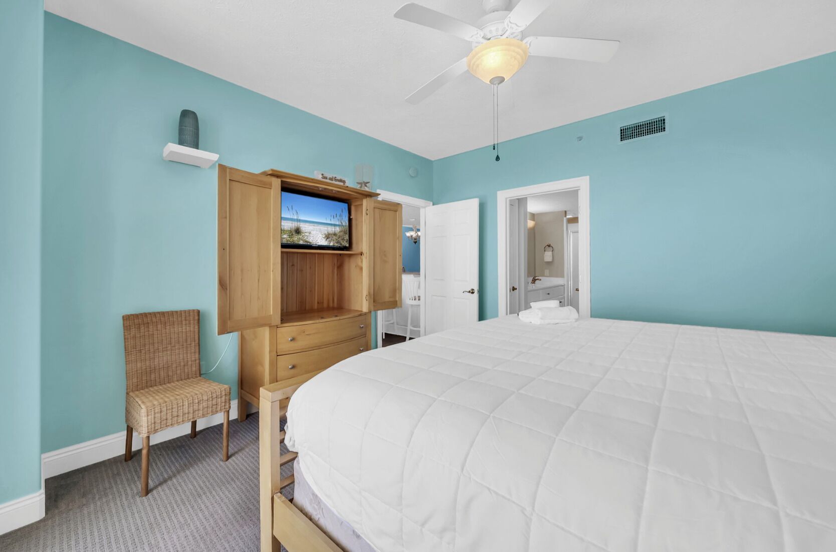 A bedroom with a bed, a TV mounted on a wooden cabinet, a chair, and a ceiling fan.