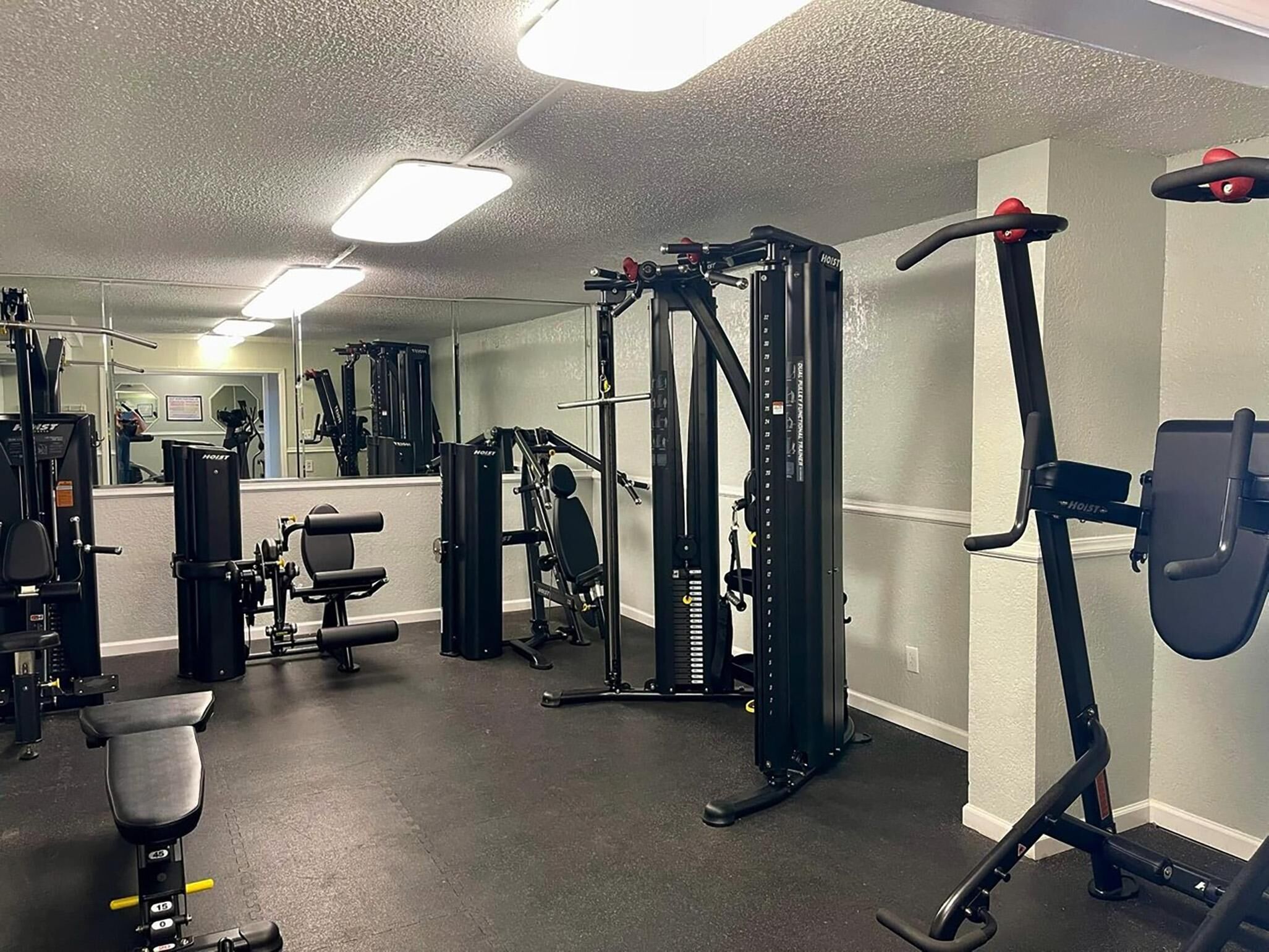A gym with various exercise equipment, including a squat rack, bench press, and cable machine.