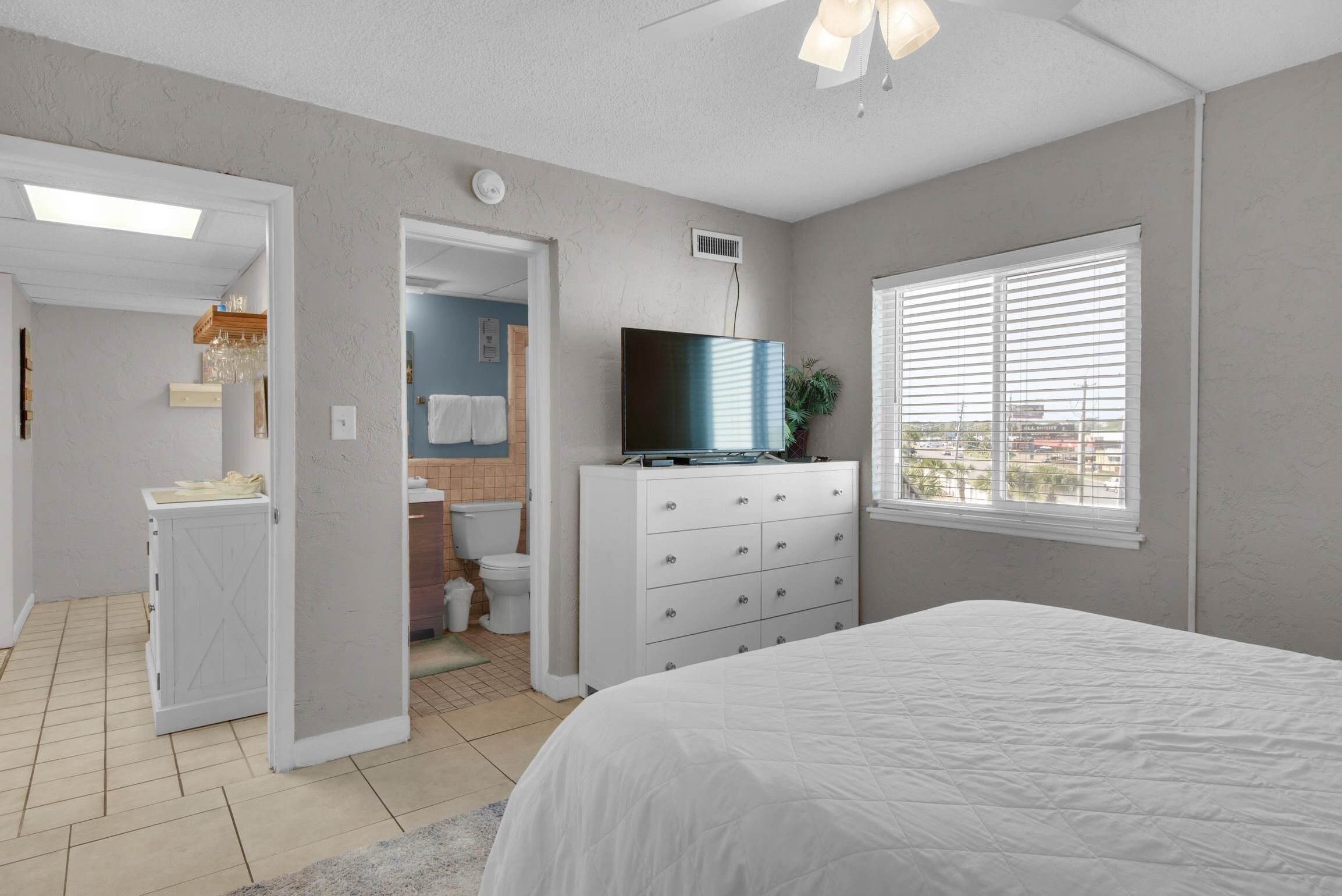 A bedroom with a bed, a dresser, a television, and a window with blinds.