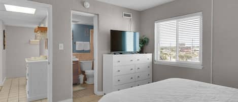 A bedroom with a bed, a dresser, a television, and a window with blinds.