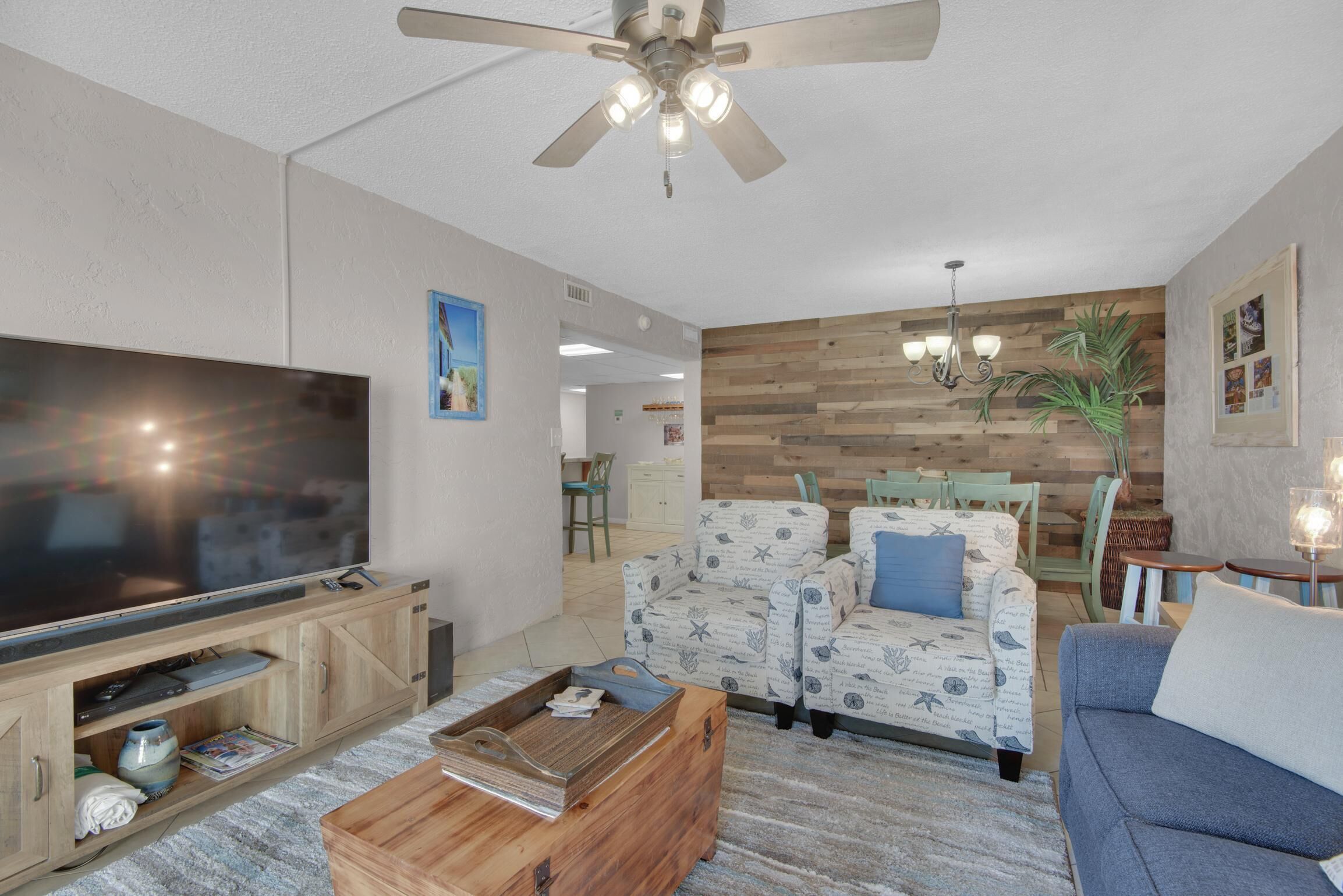 A living room with a flat-screen TV, wooden coffee table, patterned sofa, and a ceiling fan.