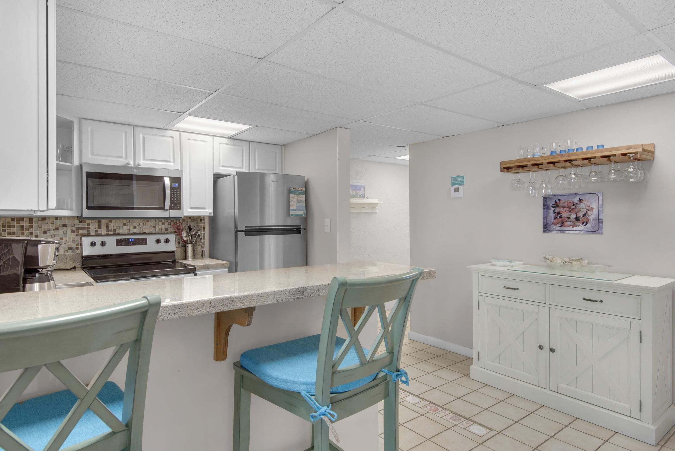 A kitchen with white cabinets, a microwave, a refrigerator, and a dining area with two chairs.