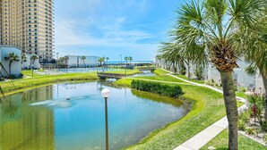 A landscaped area with a pond, palm trees, and a bridge. - Sugar Beach C-2 (Panama City Beach)