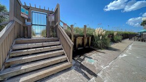A wooden staircase leading to a gated entrance with a clear sky and vegetation around. - Sugar Beach C-2 (Panama City Beach)