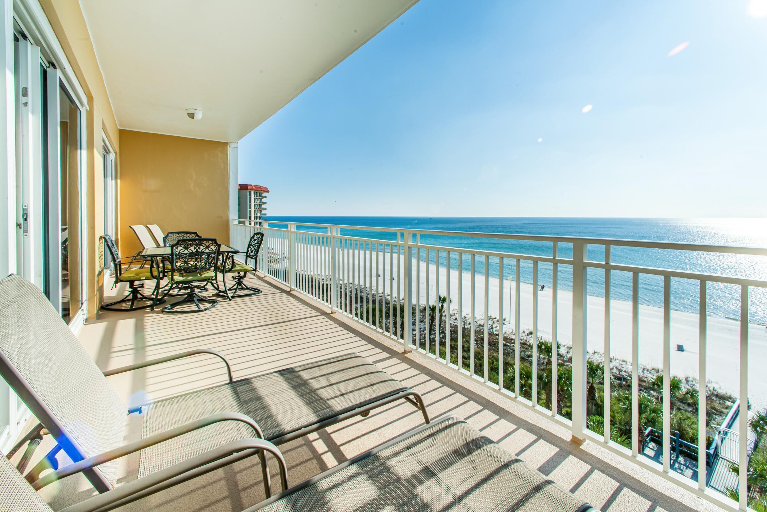 Een balkon met uitzicht op het strand, een tafel met stoelen en een hekwerk.