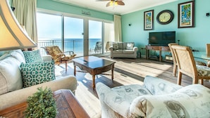 A spacious living room with a balcony, a ceiling fan, a television, and a dining area.