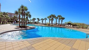 A swimming pool with palm trees and lounge chairs, surrounded by a tiled deck.