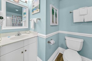 Bathroom features a white sink, toilet, and vanity with a cabinet, along with framed artwork and a towel rack.
