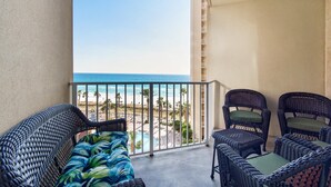 A balcony with wicker furniture, a view of the beach, and a pool.