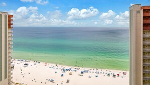 A beach view from a high-rise hotel with a sandy beach, umbrellas, and clear blue water.