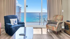 A room with a balcony, a blue armchair, a patterned armchair, a wooden coffee table, and a cabinet.