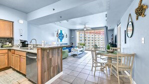 A modern kitchen with a central island, a dining area with a round table and chairs, and a living room with a sofa and a coffee table. - Shores of Panama 1816 (Panama City Beach)