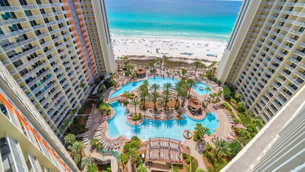 A high-rise hotel with a central pool surrounded by palm trees and a beach view. - Shores of Panama 1816 (Panama City Beach)