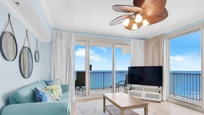 A living room with a large TV, a sofa, a coffee table, and a balcony with a view of the sea. - Shores of Panama 1401 (Panama City Beach)