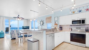 A modern kitchen with a large island, white cabinetry, and a view of the ocean. - Shores of Panama 1401 (Panama City Beach)
