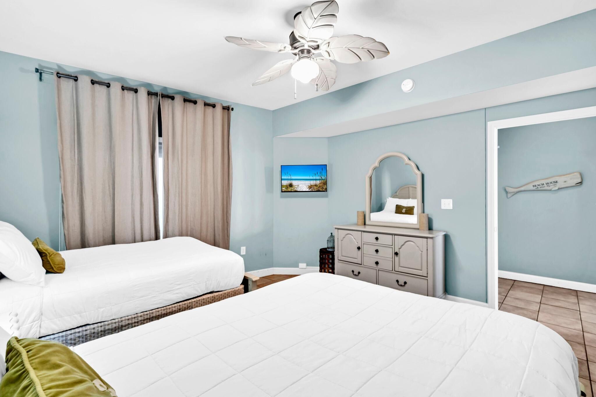 A bedroom with two beds, a ceiling fan, a dresser, and a framed picture of a beach scene.
