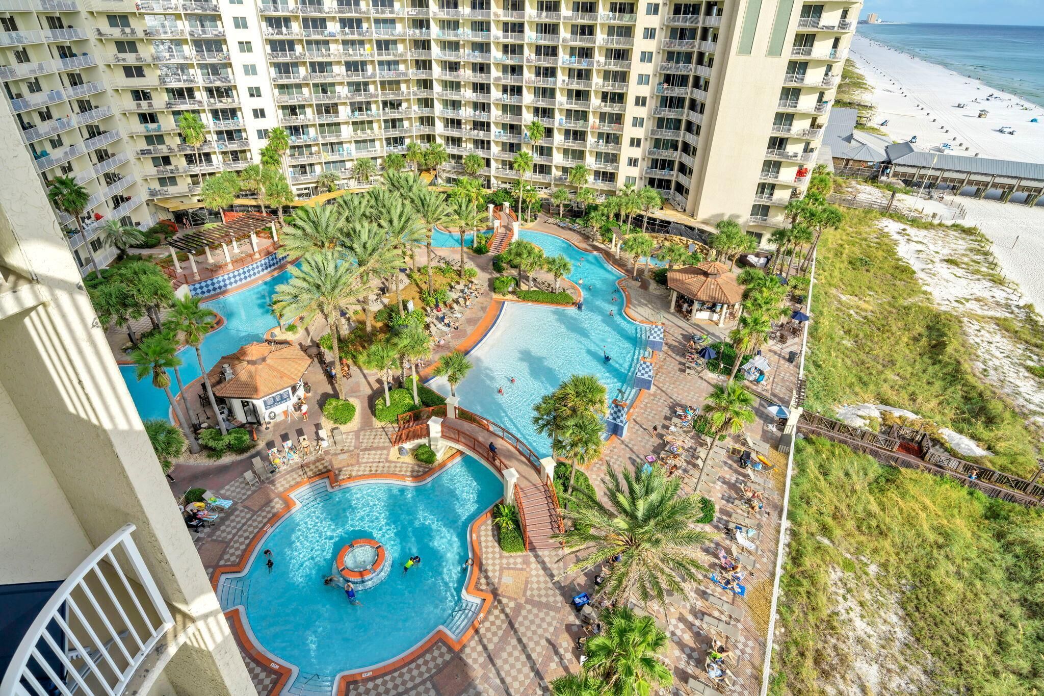 Un hôtel de grande hauteur doté d’une vaste piscine extérieure, entourée de palmiers et agrémentée d’espaces de détente.