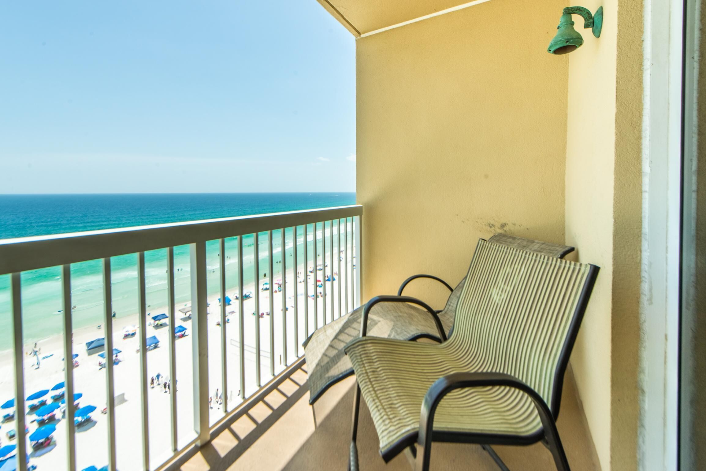 Ein Balkon mit Blick auf einen Strand, ein Stuhl und eine Wandleuchte.