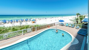 A pool area with a view of the beach, lounge chairs, and umbrellas.