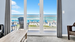 Une pièce avec une table en bois, une chaise en osier et une vue sur la plage, visible à travers une porte-fenêtre coulissante.