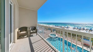 Un balcon avec deux fauteuils en osier, un espace piscine avec un jacuzzi, et une vue sur la plage et l’océan.