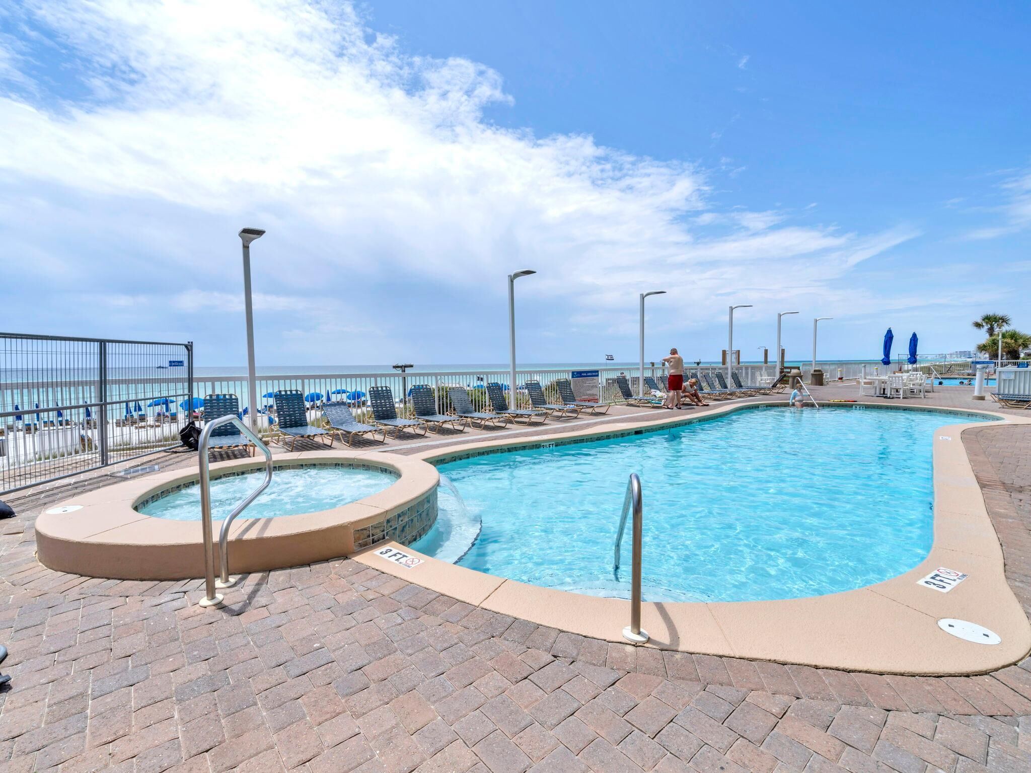 A swimming pool with a hot tub, lounge chairs, and a view of the ocean.