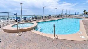A rectangular swimming pool with a hot tub section, surrounded by lounge chairs and umbrellas, with a view of the ocean. - Seychelles 1504 (Panama City Beach)