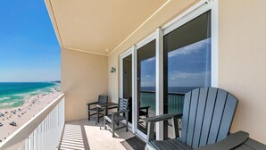 A balcony with a view of the beach, a table, two chairs, and a single lounge chair. - Seychelles 1504 (Panama City Beach)