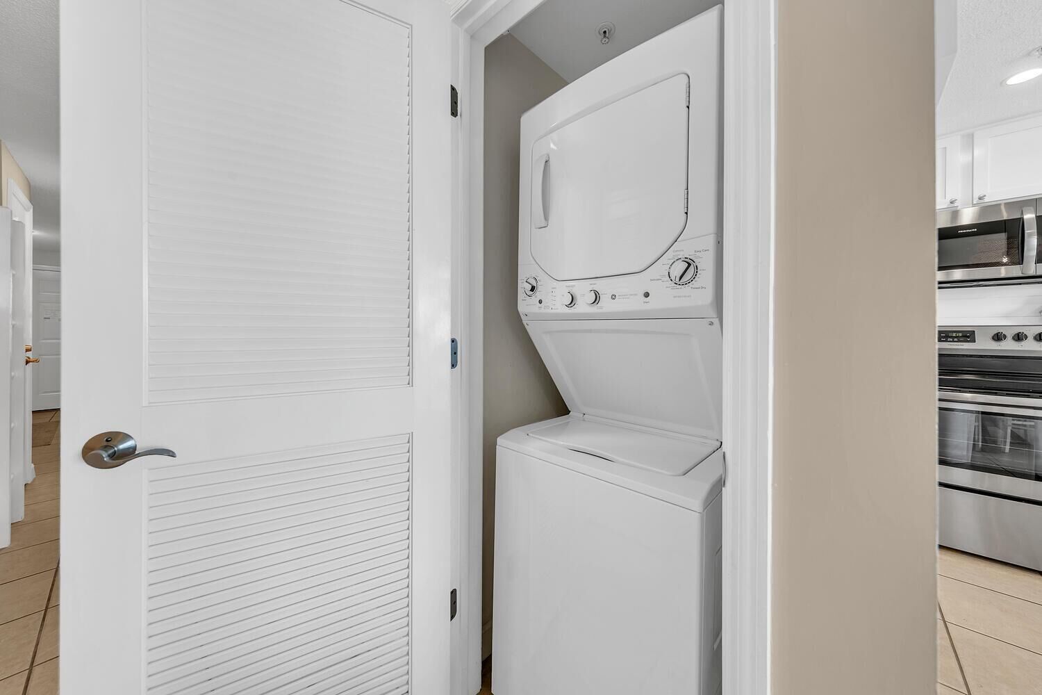 A compact laundry room with a built-in washer and dryer, adjacent to a kitchen area with stainless steel appliances.