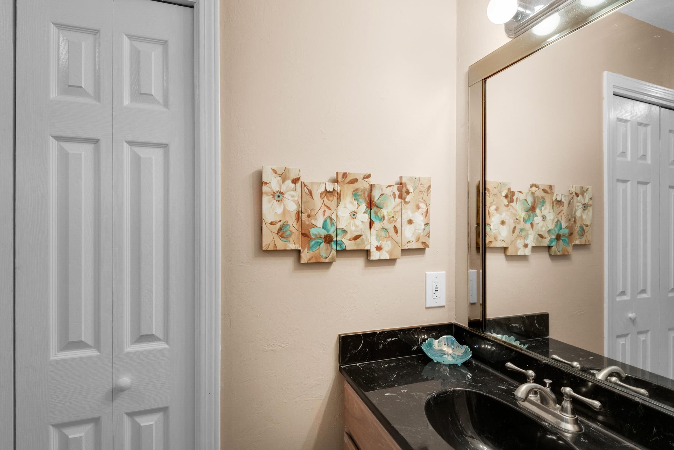 A bathroom with a black marble sink, a mirror, and floral artwork on the wall.