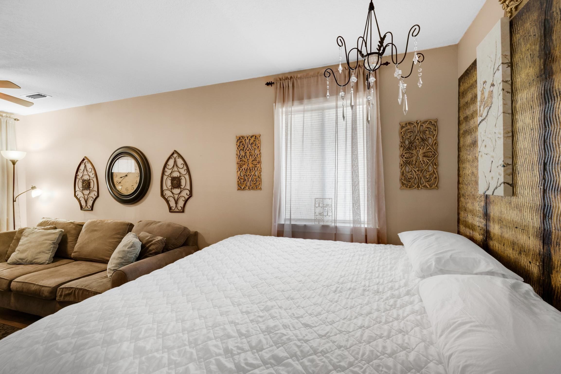 Een slaapkamer met een groot bed, een bank, decoratieve wandkunst en een kroonluchter.